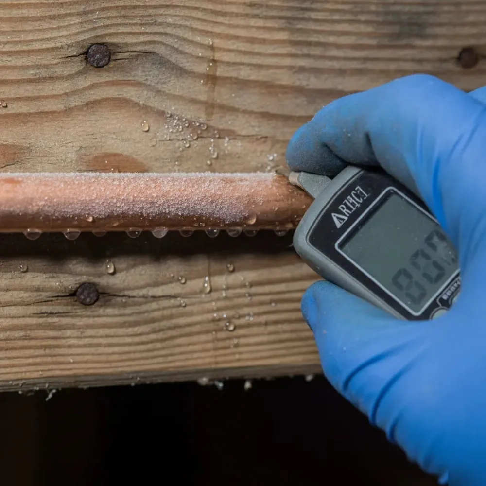 Frost-covered copper pipe being checked with a digital thermometer