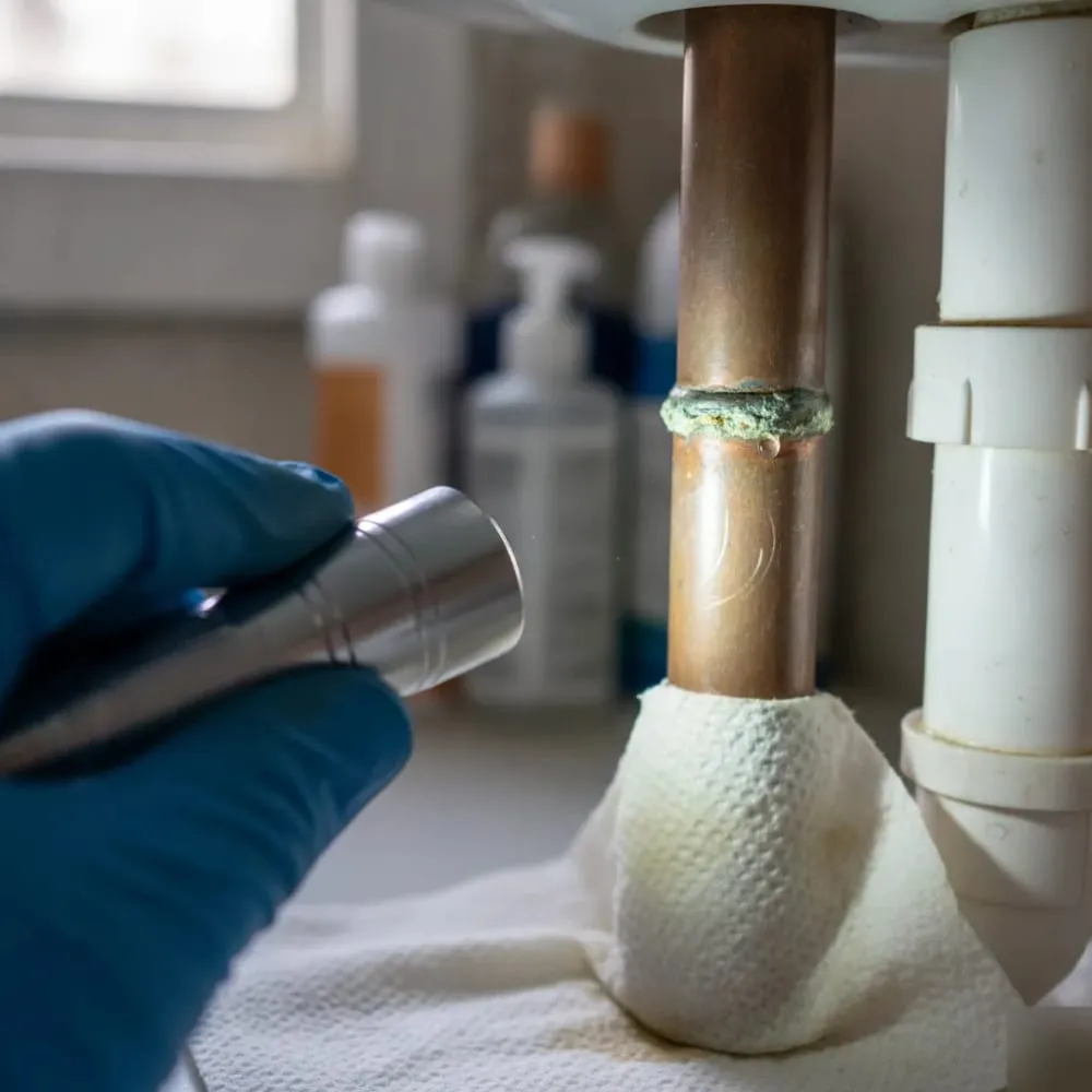 Close-up of a small corroded joint on a copper pipe under a sink